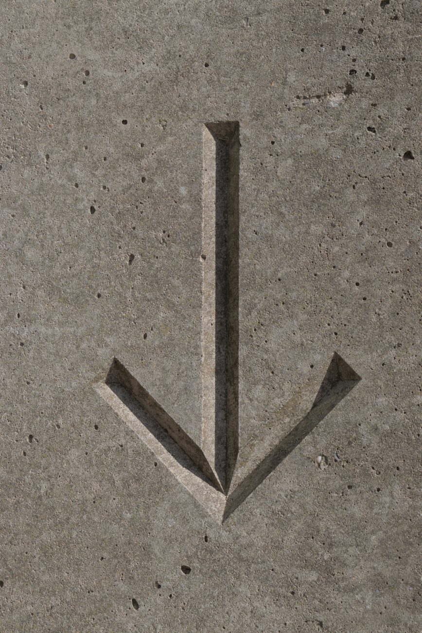 A carved concrete arrow pointing down — a sign out of context
